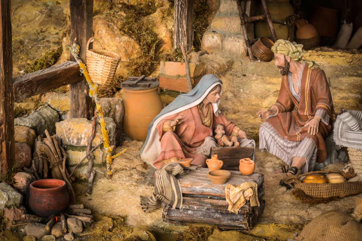 A miniature diorama depicts two figures seated near a small infant in a rustic, straw-filled setting with pottery.