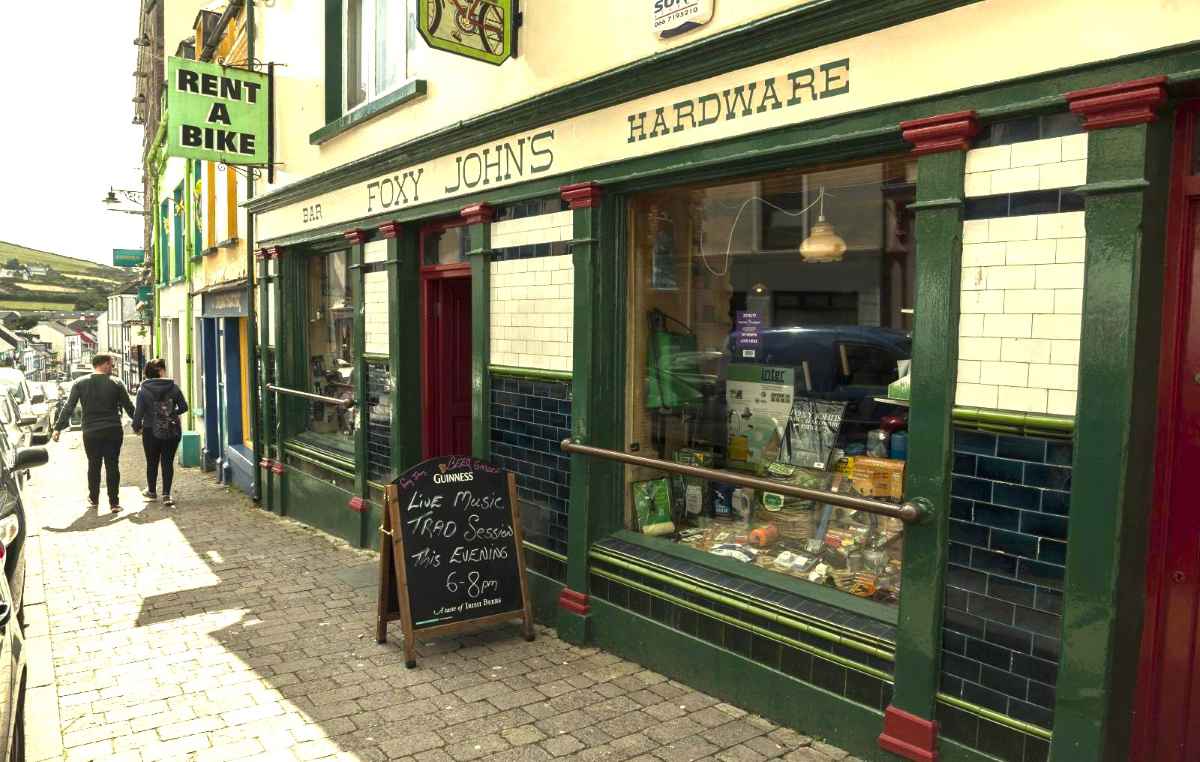 A storefront labeled Foxy Johns Bar and Hardware features a sidewalk sign advertising live music on a cobblestone street.