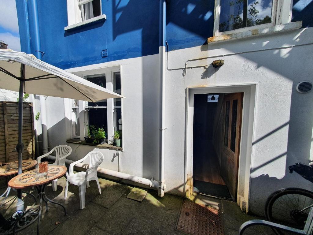 A patio with white plastic chairs and a small table sits outside a building with blue and white exterior walls.