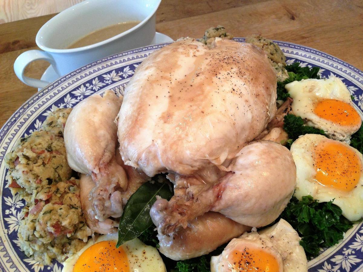 A roasted chicken is served on a patterned plate with fried eggs, stuffing, and a side of gravy.