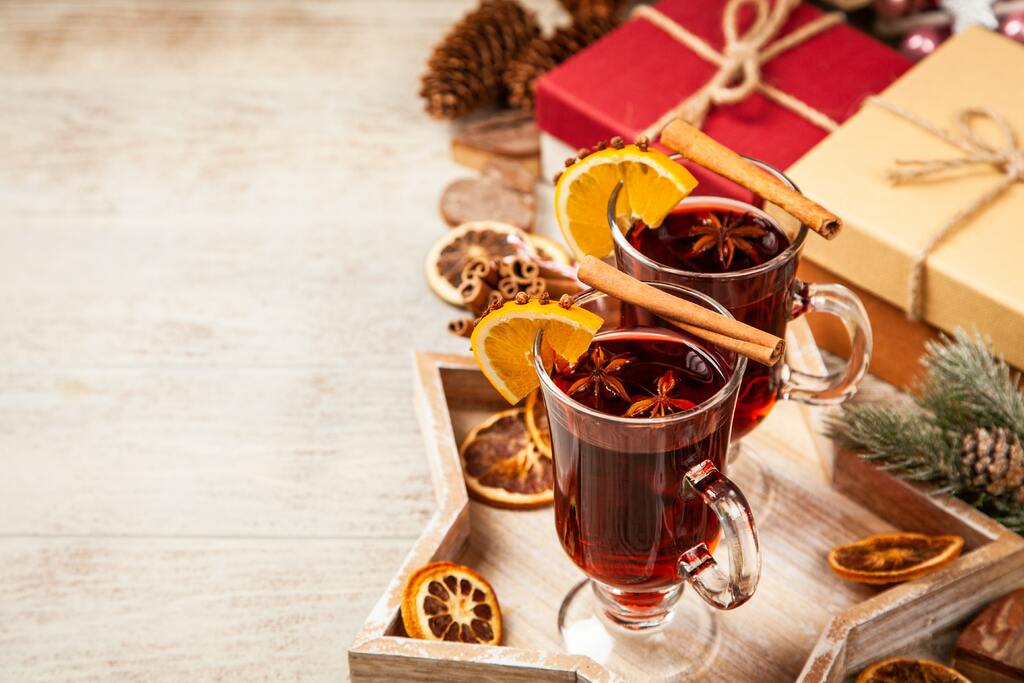 Two glass mugs of mulled wine garnished with orange slices, cinnamon sticks, and star anise sit on a wooden star tray.