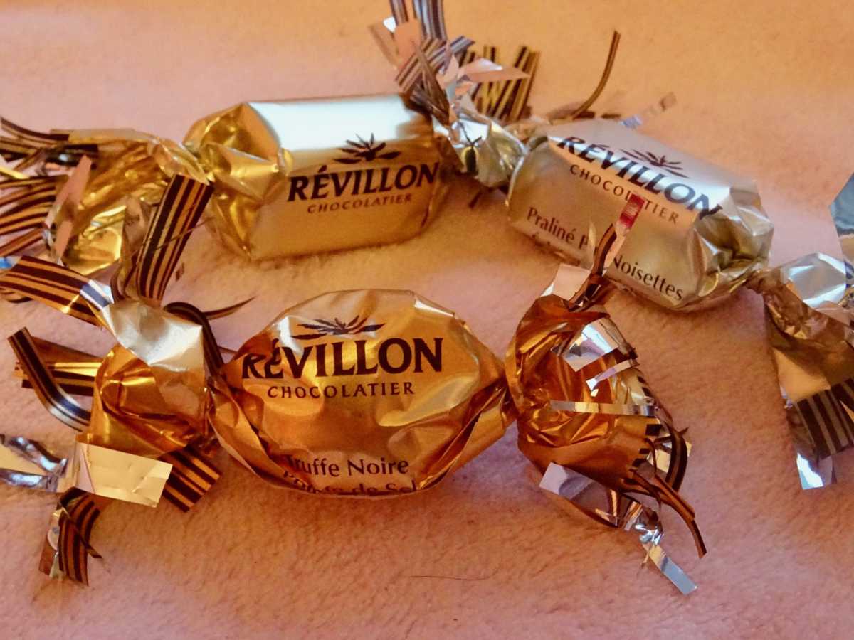 Three gold-wrapped chocolate candies with the brand name Révillon Chocolatier printed on the wrappers.