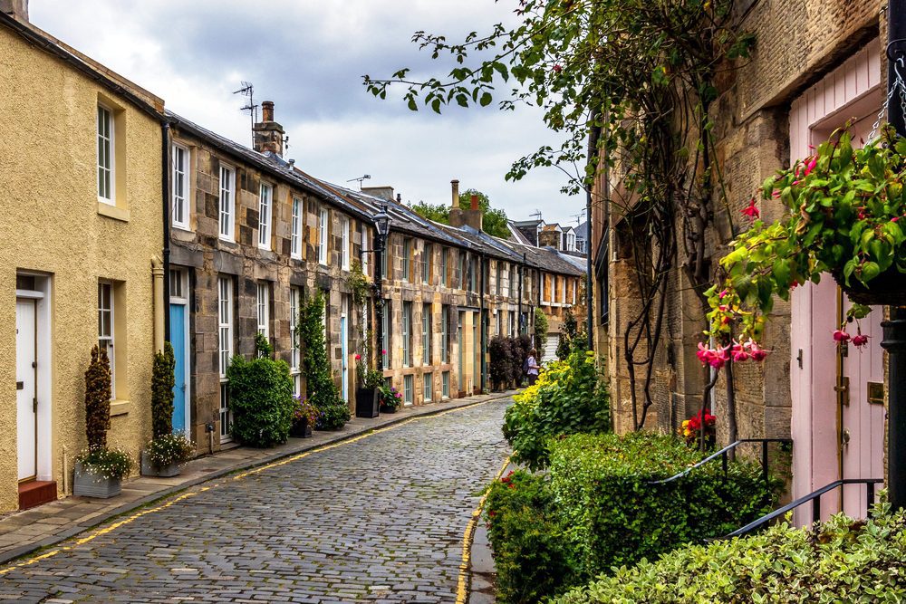 Circus Lane Edinburgh a curved cobblestone street fronted by small Mews cottages with flowers and roses climbing the walls of the cottages