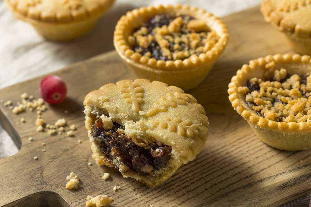 Mincemeat pies on a wooden platter. Mincemeat shows on one pie cut in half