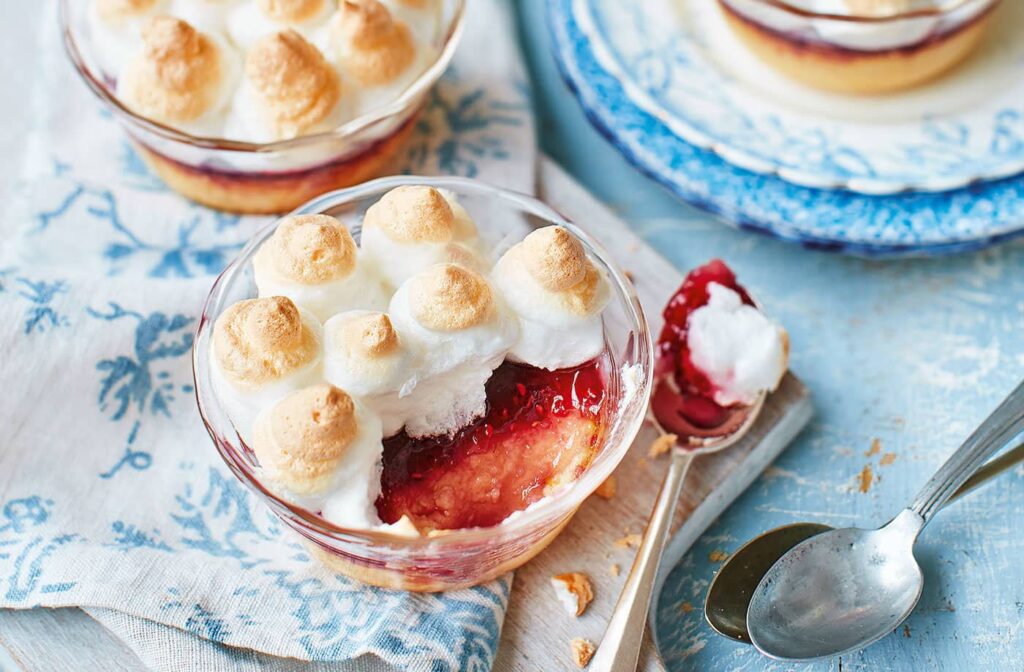 Queen of puddings a strawebbery base is topped with meringue and served in a round bowl