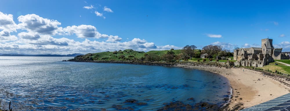 Inchcolm Abbey on the island sits as a grey sstone ruin a few yards from a yellow sandy beach.