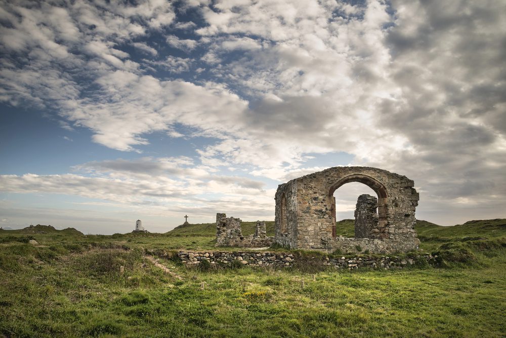 A ruined church on Llanddwyn Island only the arch and half walls still stands you can see the Stouth Stack lighthouse in the distance and also a cross