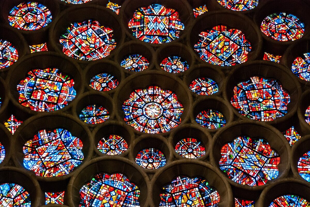 A pattern of circular stained glass windows with geometric red, blue, and yellow designs set into a stone wall.
