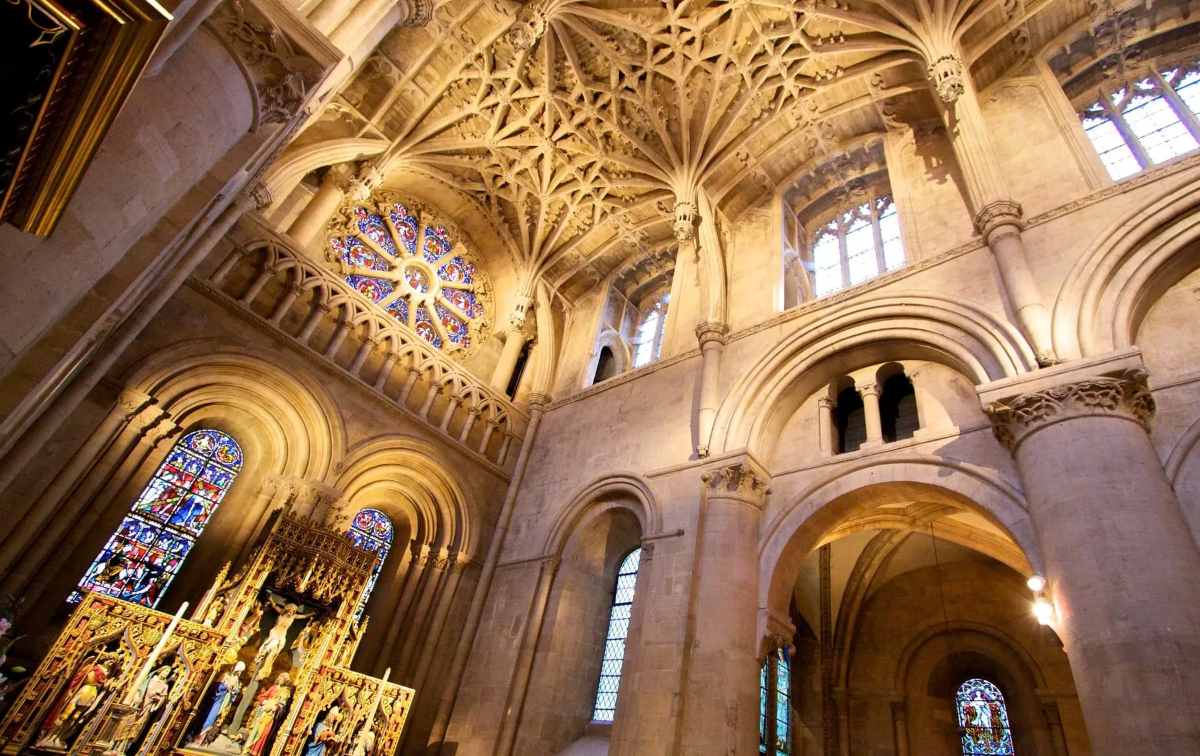 The interior of a stone church features vaulted ceilings, arched windows with stained glass, and an ornate golden altar.