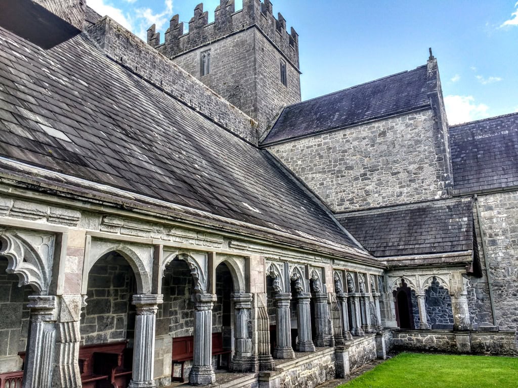 The curved arches of the greay stone Holy Cross Abbey in Ireland surround a green patch of lawn in the centre of the Abbey