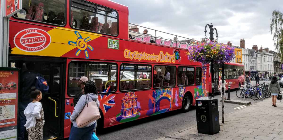 A red double-decker tour bus is parked on a city street with people boarding near a sidewalk.