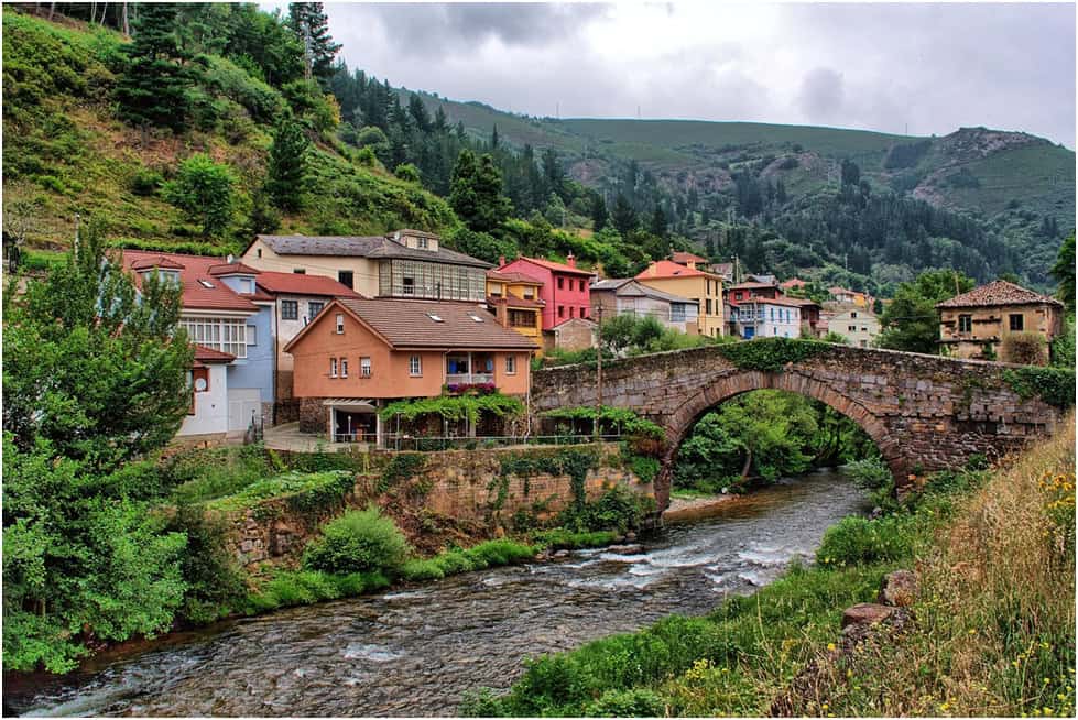 The village of Luarca in Asturias this colourful village site4s below a gren rolling hill in the foreground is an ancient arched bridge