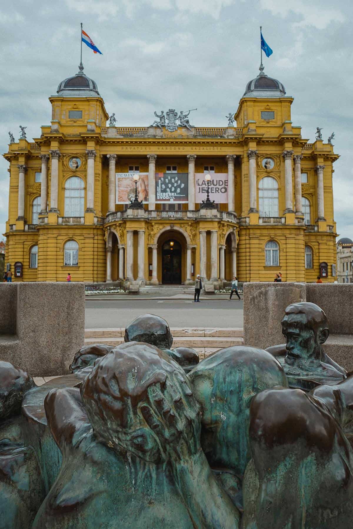 Majestic yellow theater and bronze sculpture in Zagreb, Croatia showcase cultural heritage.