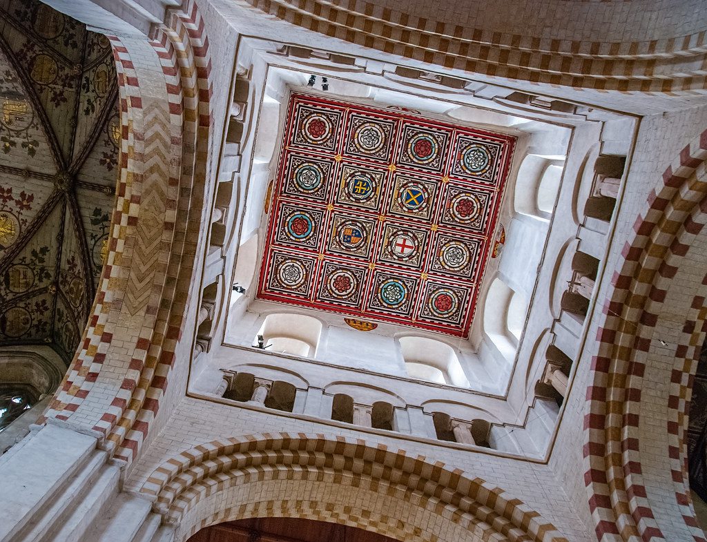 A low-angle view of a vaulted stone ceiling featuring a central square panel with colorful, patterned geometric designs.