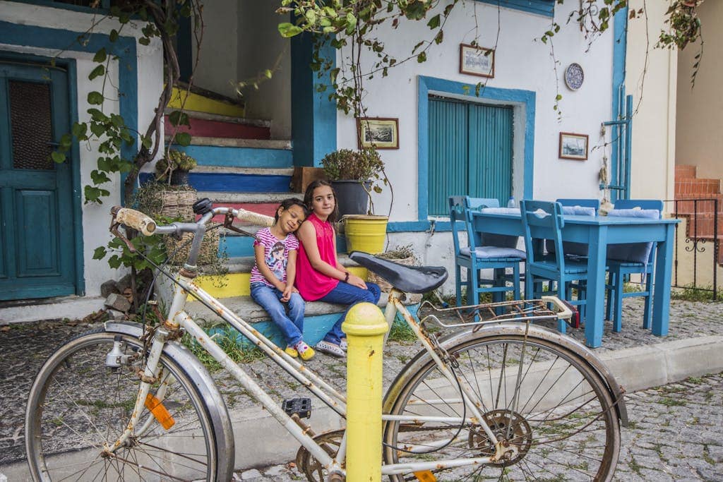 Two children relax by colorful steps next to a rustic bike, embraced by vibrant visuals and calm ambiance.