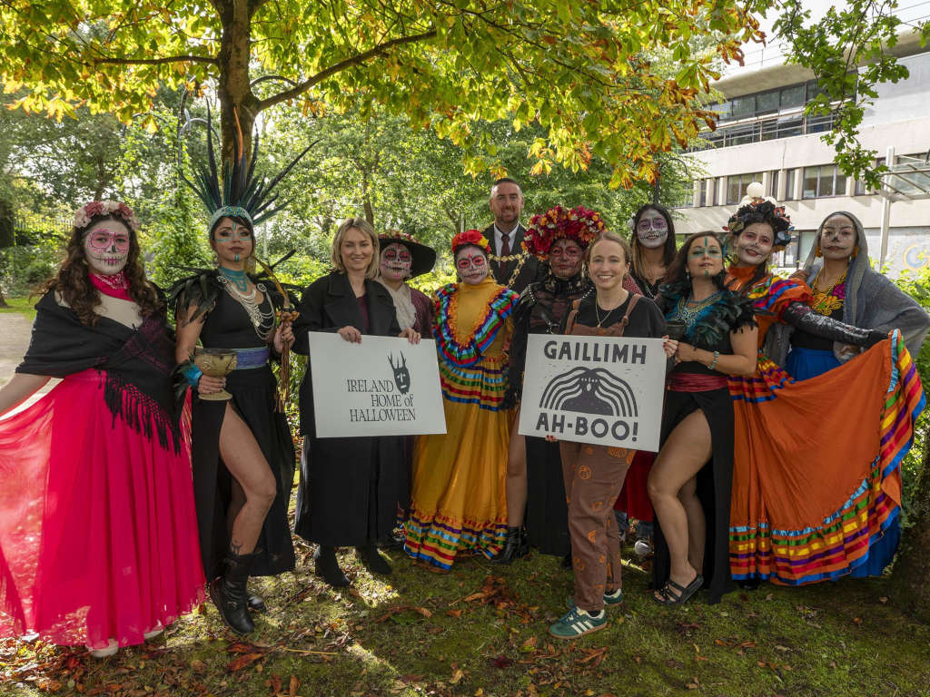 A group of people in colorful Halloween costumes hold signs promoting Ireland as the home of Halloween in Galway.