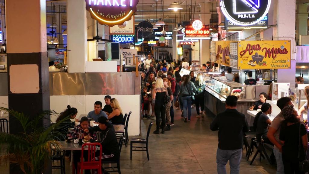 Grand central market street lunch shops with diversity of glowing retro neon signs. Multiracial people on foodcourt. Citizens dining with fast food in LA.