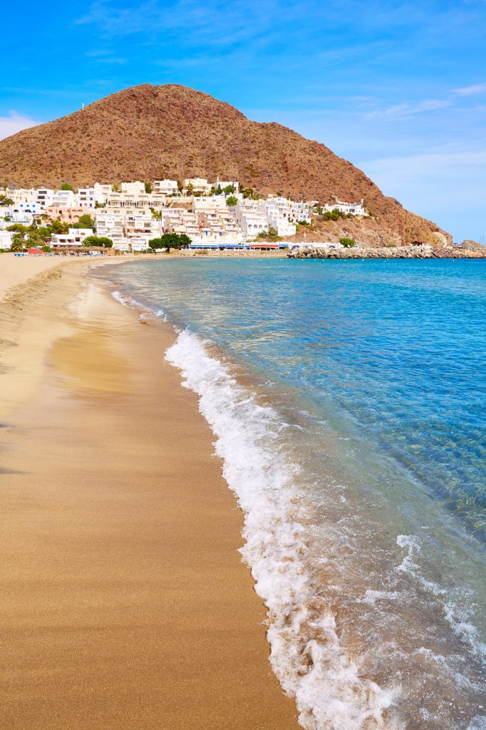 The Cabo de Gata national Park in Almeria. A golden sand beach spreads out before a small hill that has a white village at its base
