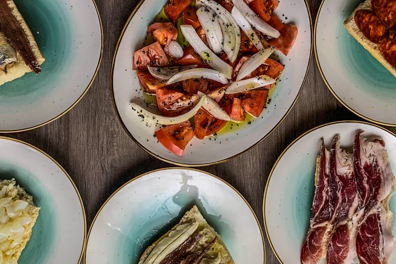 Aerial view of eclectic Spanish tapas spread on elegant ceramic plates.
