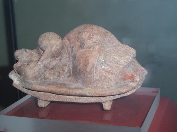 A small, limestone statuette (approx. 12 cm tall) discovered in the Ħal Saflieni Hypogeum, a subterranean Neolithic burial complex. The figure is carved from globigerina limestone and depicts a stylized, corpulent human form—likely female—with exaggerated hips and thighs.