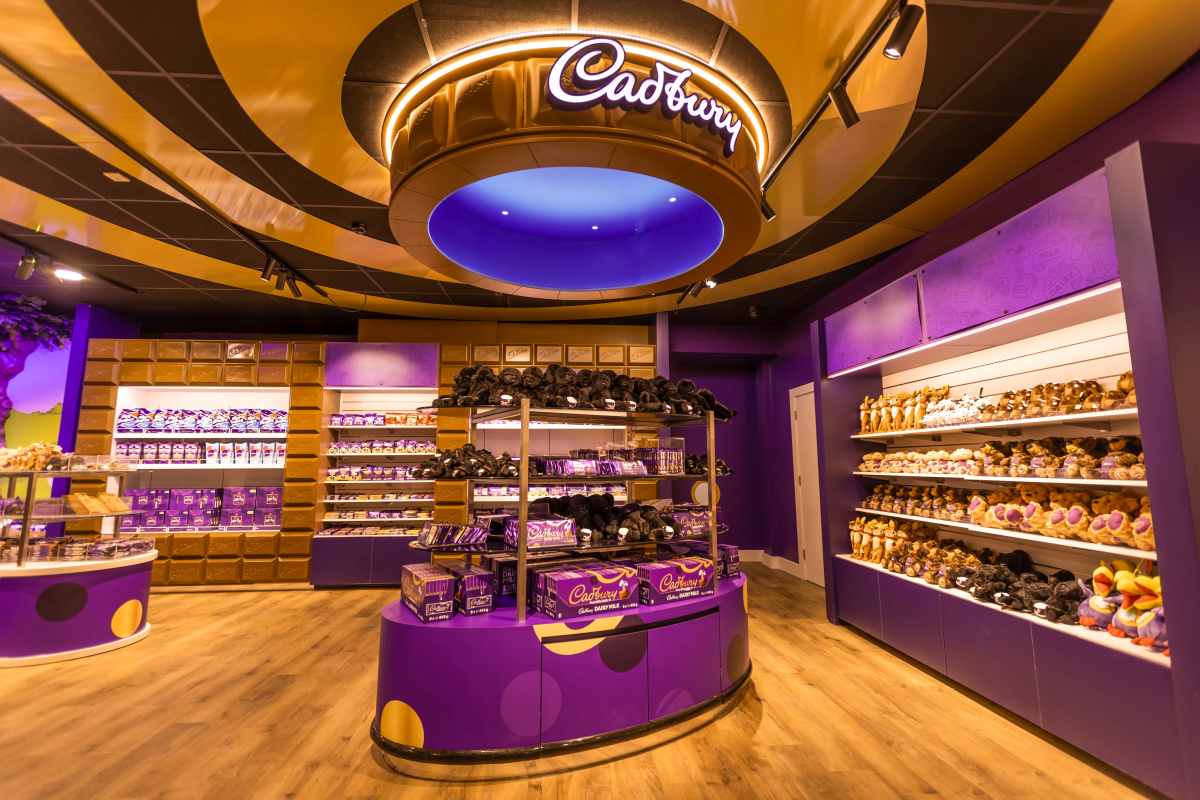 A retail store interior features shelves stocked with Cadbury chocolate products and plush toys under a circular ceiling