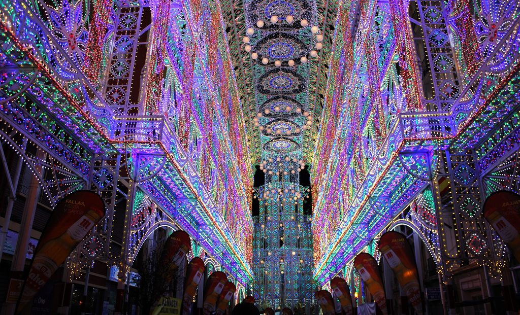 A street is lined with tall, intricate metal structures covered in dense, multi-colored LED light displays at night.