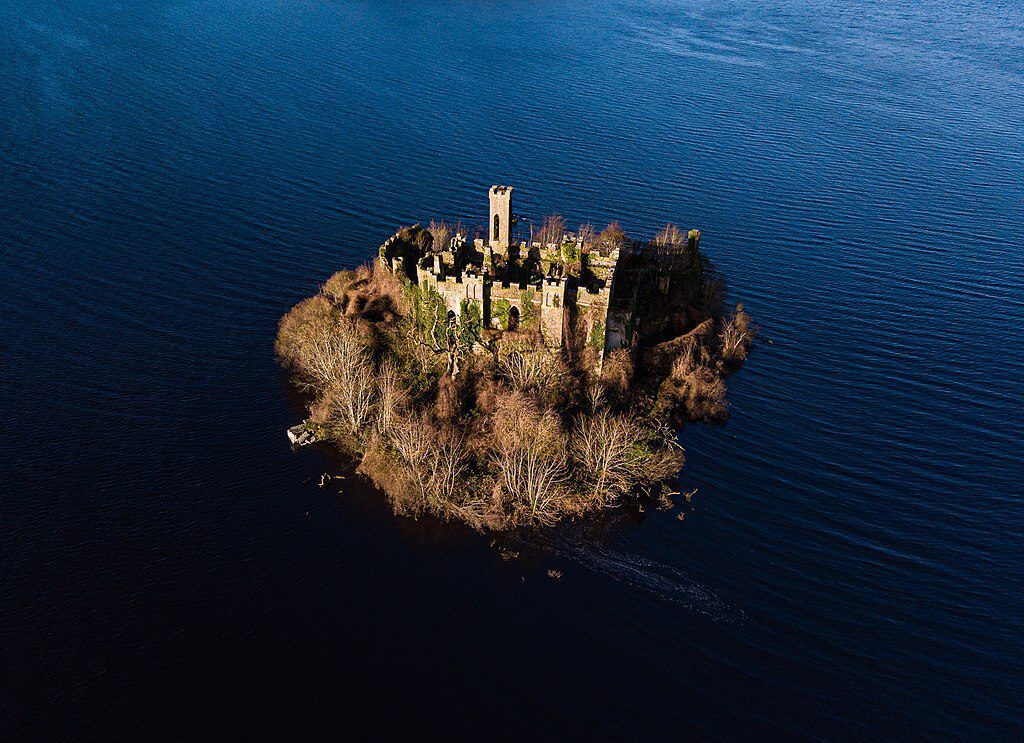 Aerial view of a ruined castle on a small island surrounded by water.
