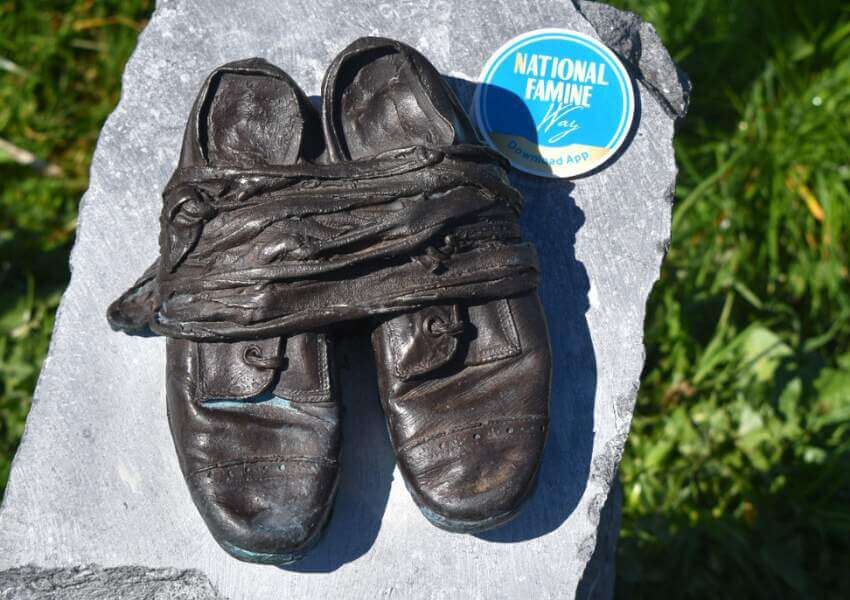Bronze shoe sculpture with cloth binding on stone with National Famine Way sticker.