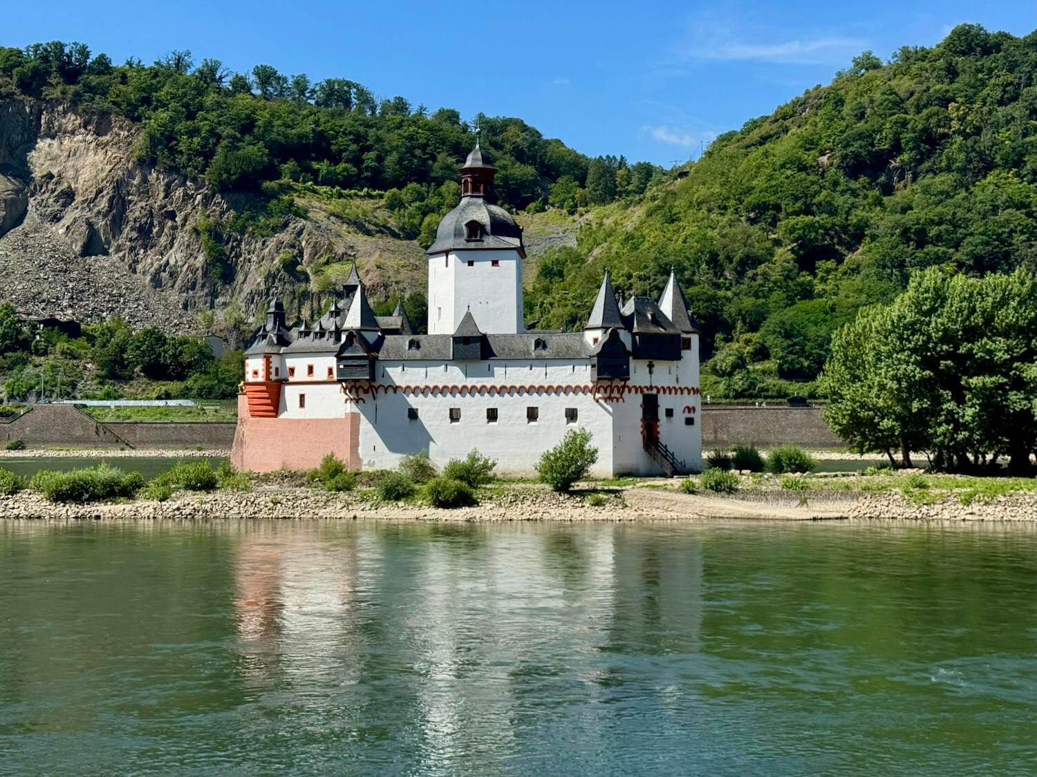 Pfalzgrafenstein Castle on the Rhine River, surrounded by lush green hills.