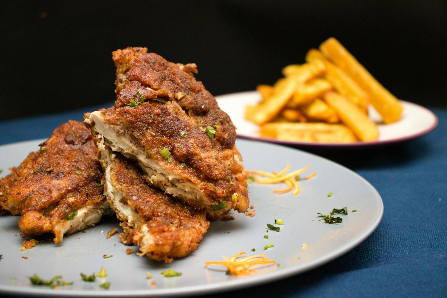 Closeup of deep fried meat chopped and served on plate on table with french fries on background