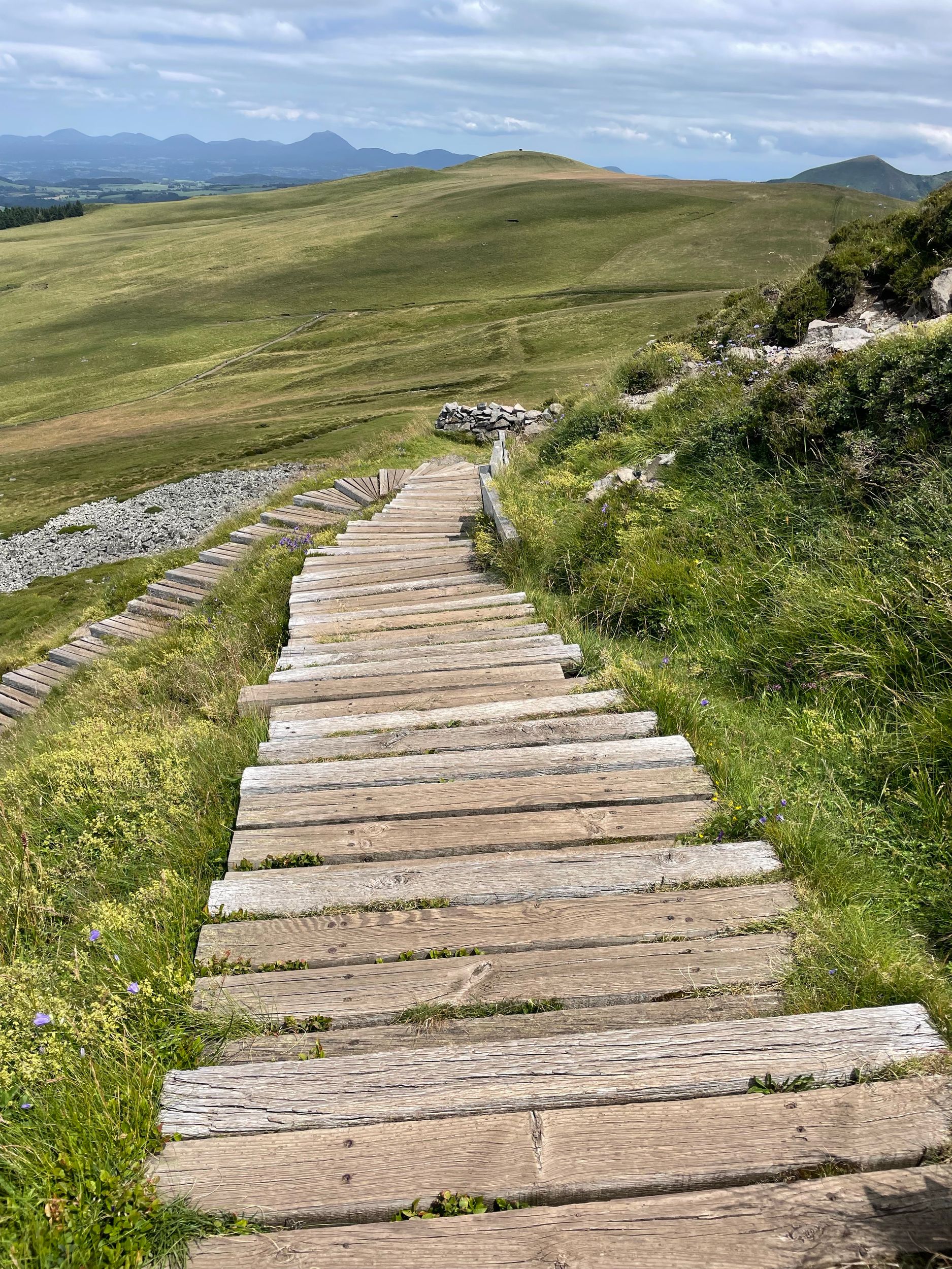 Explore serene landscapes with a rustic wooden boardwalk guiding your journey through lush green hills.