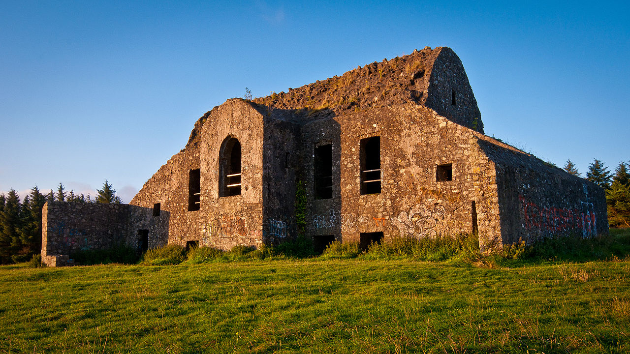 Graffiti-covered stone ruins of the Hellfire Club on Montpelier Hill, Dublin, Ireland, bathed in golden light.