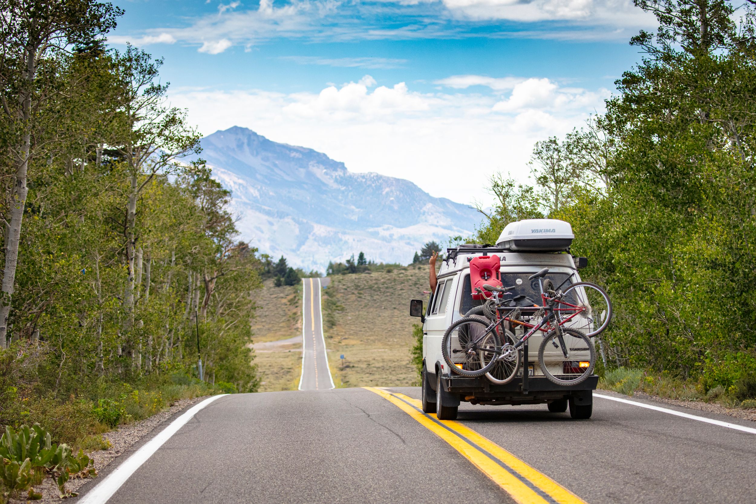 A camper van travels through a beautiful mountain landscape, bicycles mounted on the back.