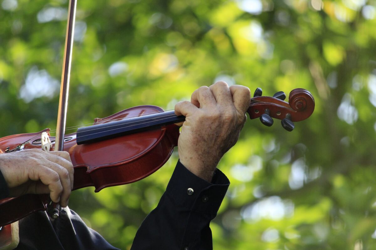 A detailed view of hands playing a violin against a vibrant outdoor background, emphasizing music.