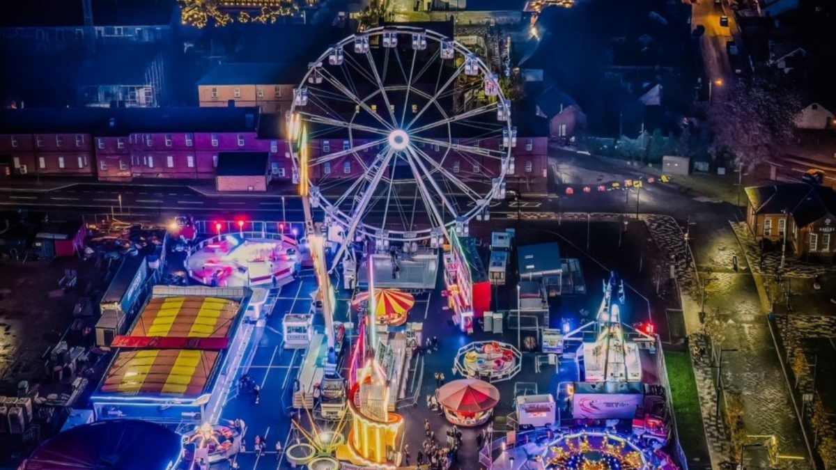 Vibrant night fair with a towering Ferris wheel and illuminated rides in a European town.
