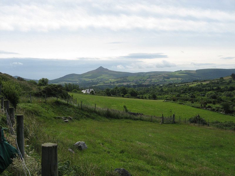 A green valley with a conical mountain in the distance under a cloudy sky.