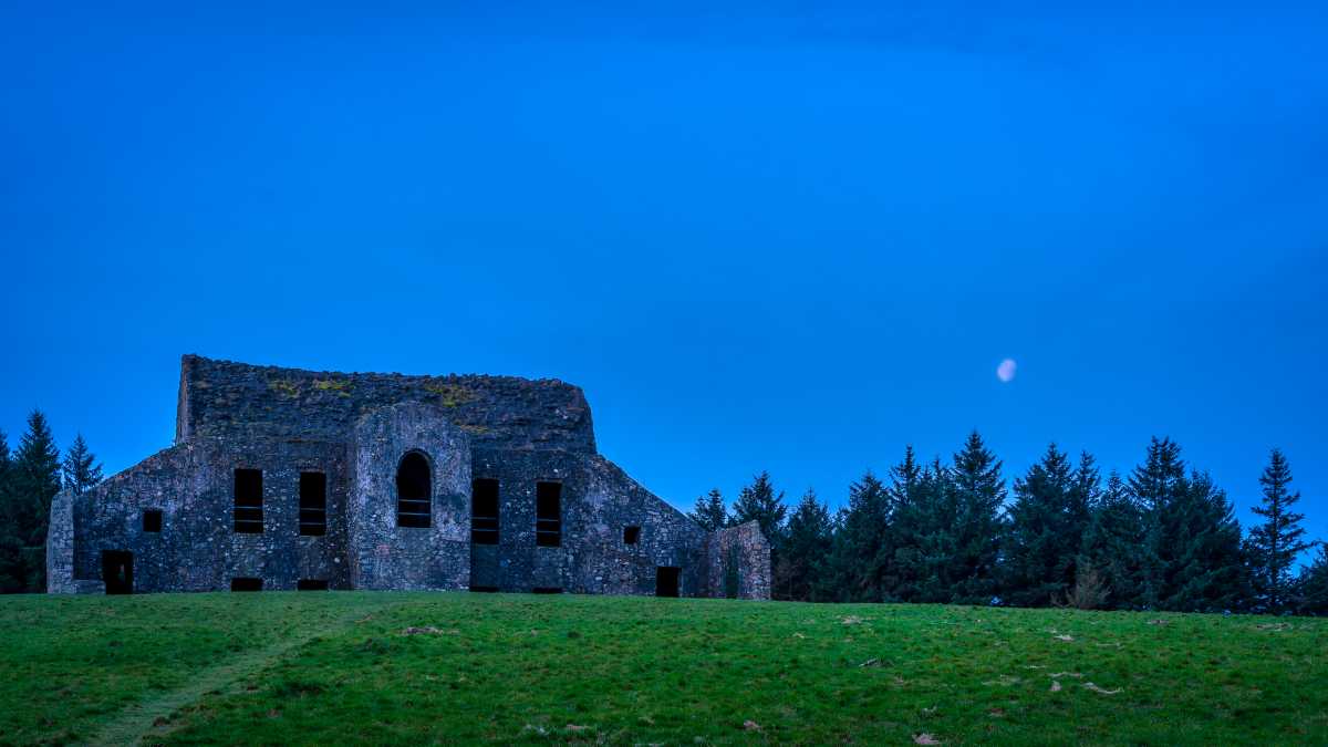 The Hellfire Club ruin stands on a grassy hill under a deep blue sky with a visible moon.