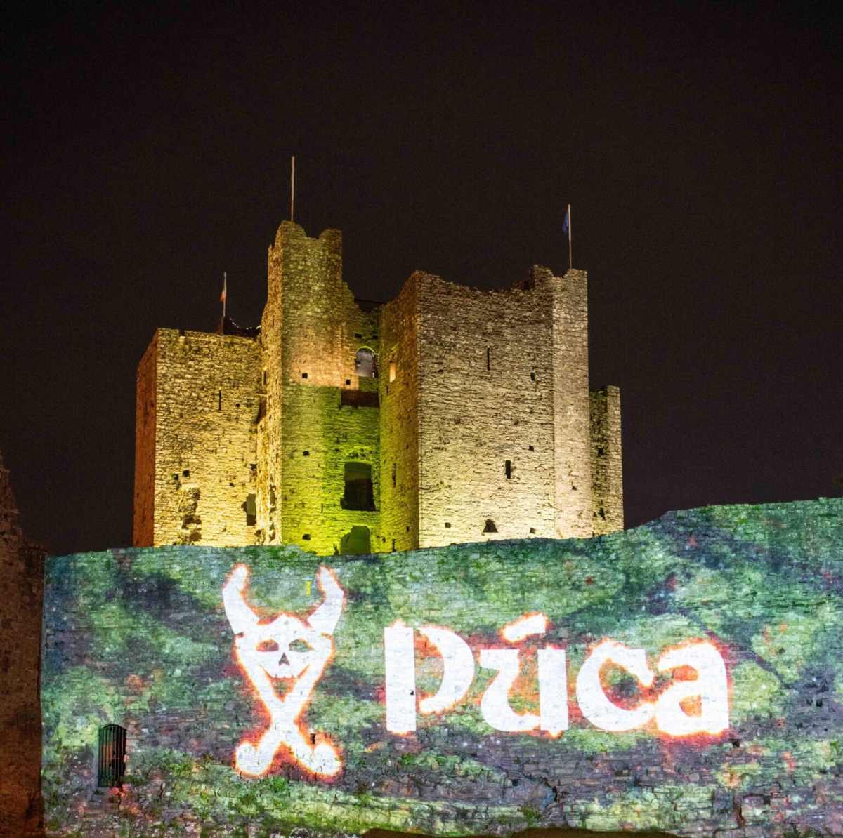 Trim Castle in Ireland illuminated at night with a Púca Festival projection on its historic walls.