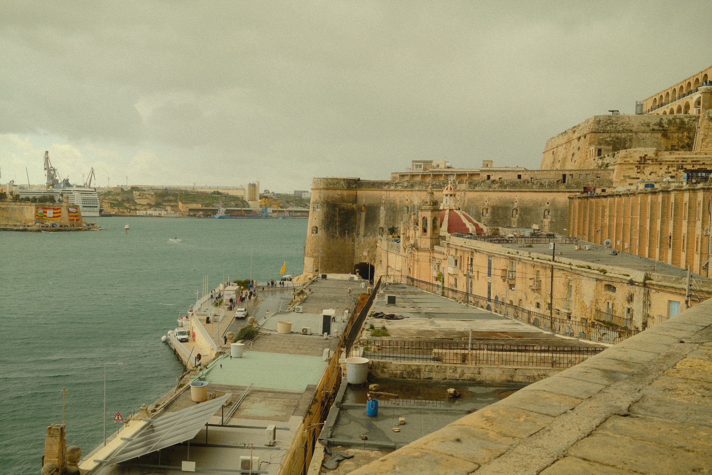 Scenic view of Malta's fortifications along the waterfront with a cruise ship in the port.