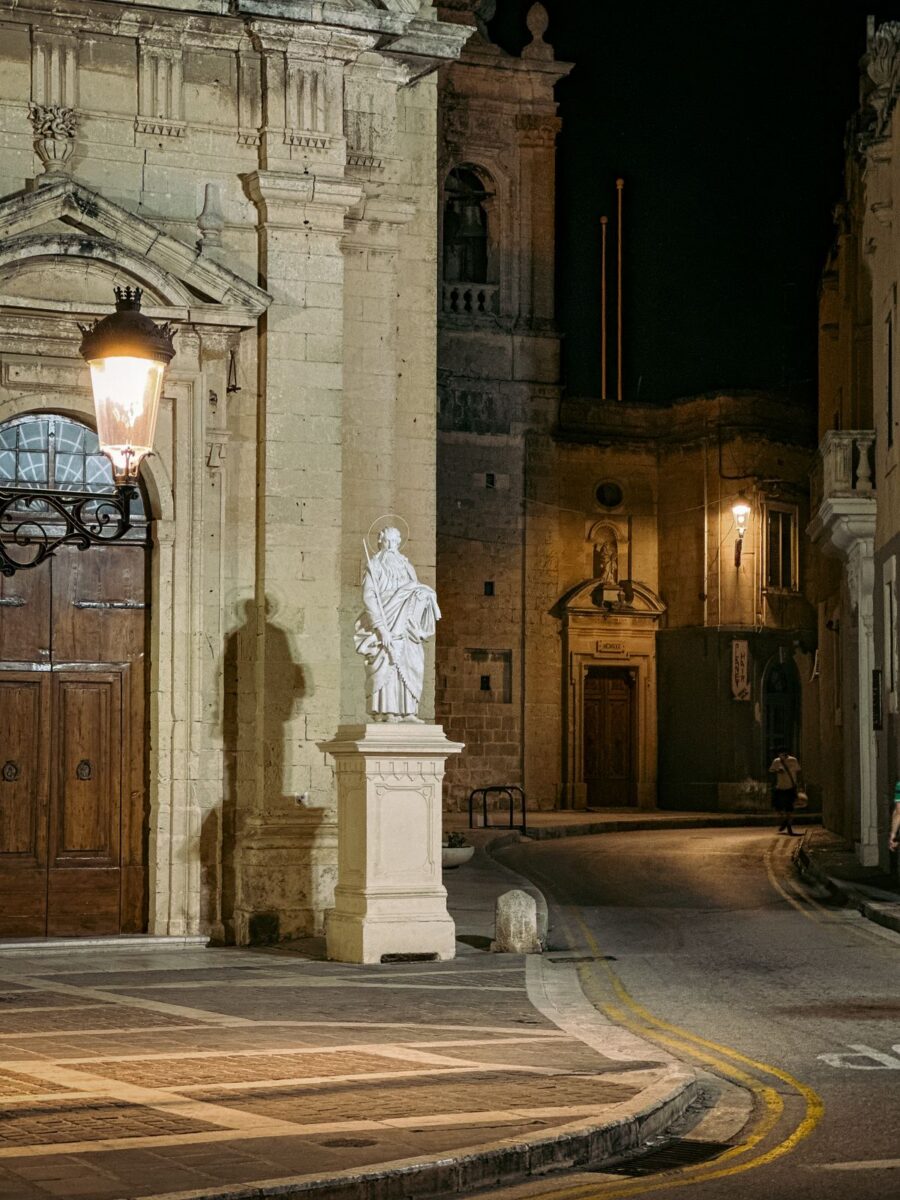 Serene night view of a historic street in Mdina, Malta featuring a prominent statue and warm lighting.