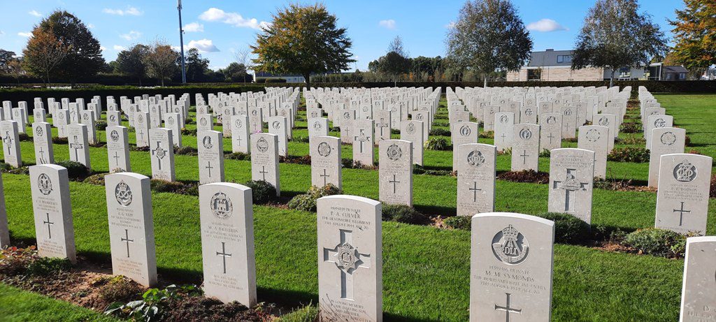 Serene rows of white headstones at Le Touret Military Cemetery in France under a blue sky.