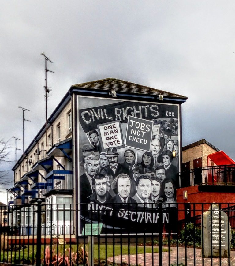 A black-and-white mural on the side of a building depicts a crowd holding signs that read Civil Rights and Jobs Not Creed.