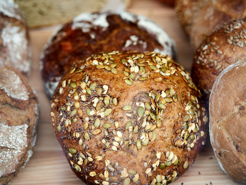 A variety of round, crusty loaves of bread topped with seeds sit on a wooden surface.