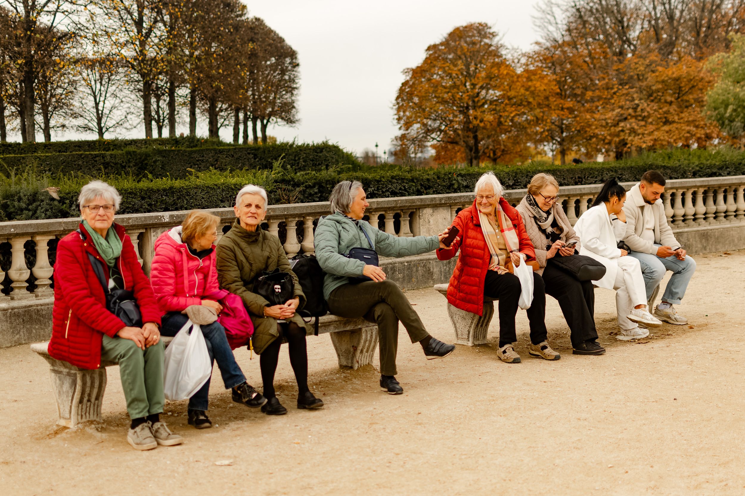 A diverse group relaxes on stone benches in Pariss Tuileries Garden amidst autumn foliage.
