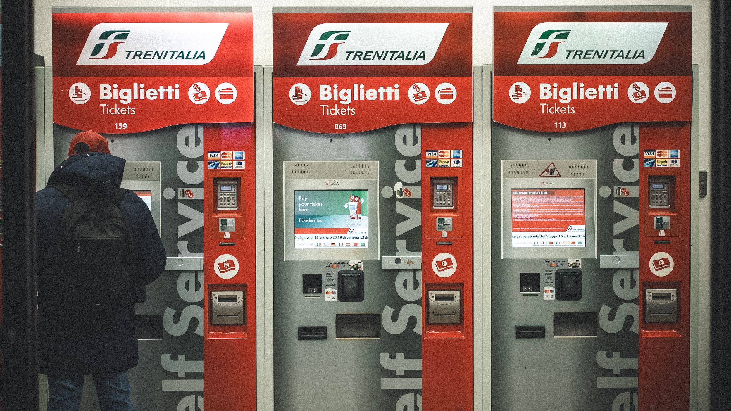 A person uses a Trenitalia self-service ticket machine in Italy.