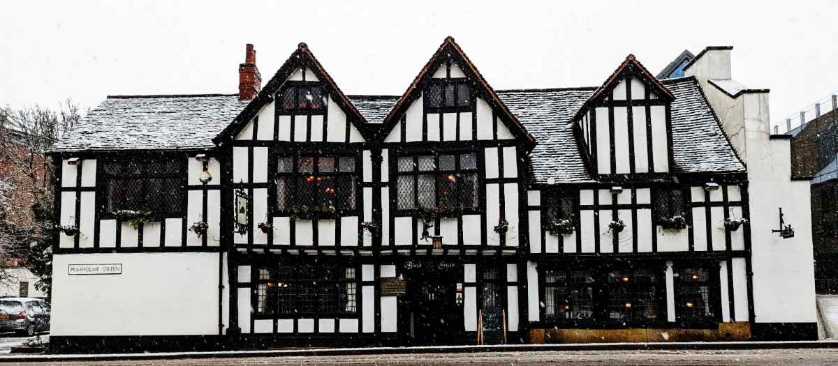 A snow-covered, timber-framed building with multiple gables stands along a street.