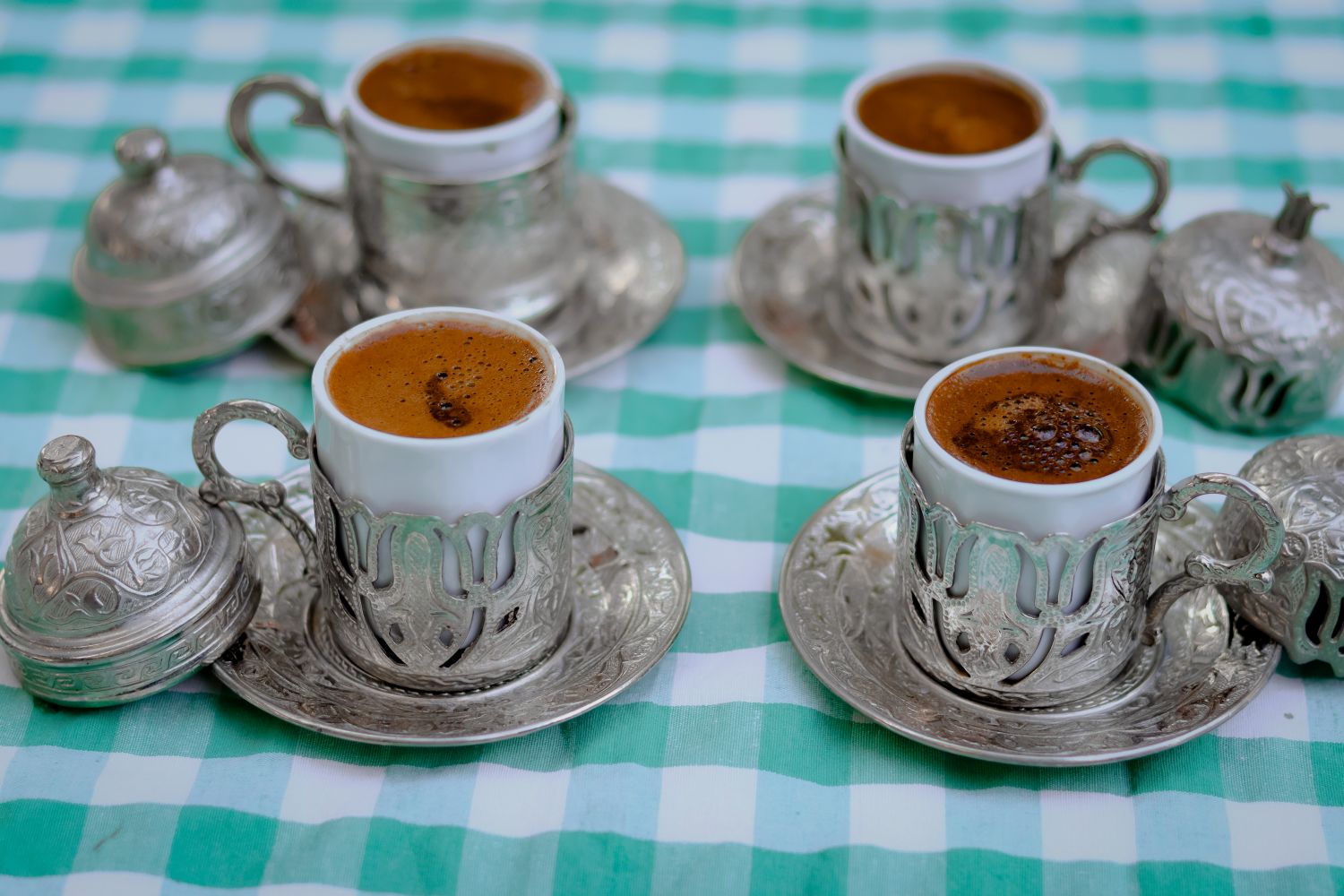 Close-up of four ornate Turkish coffee cups and saucers on a green checkered tablecloth.