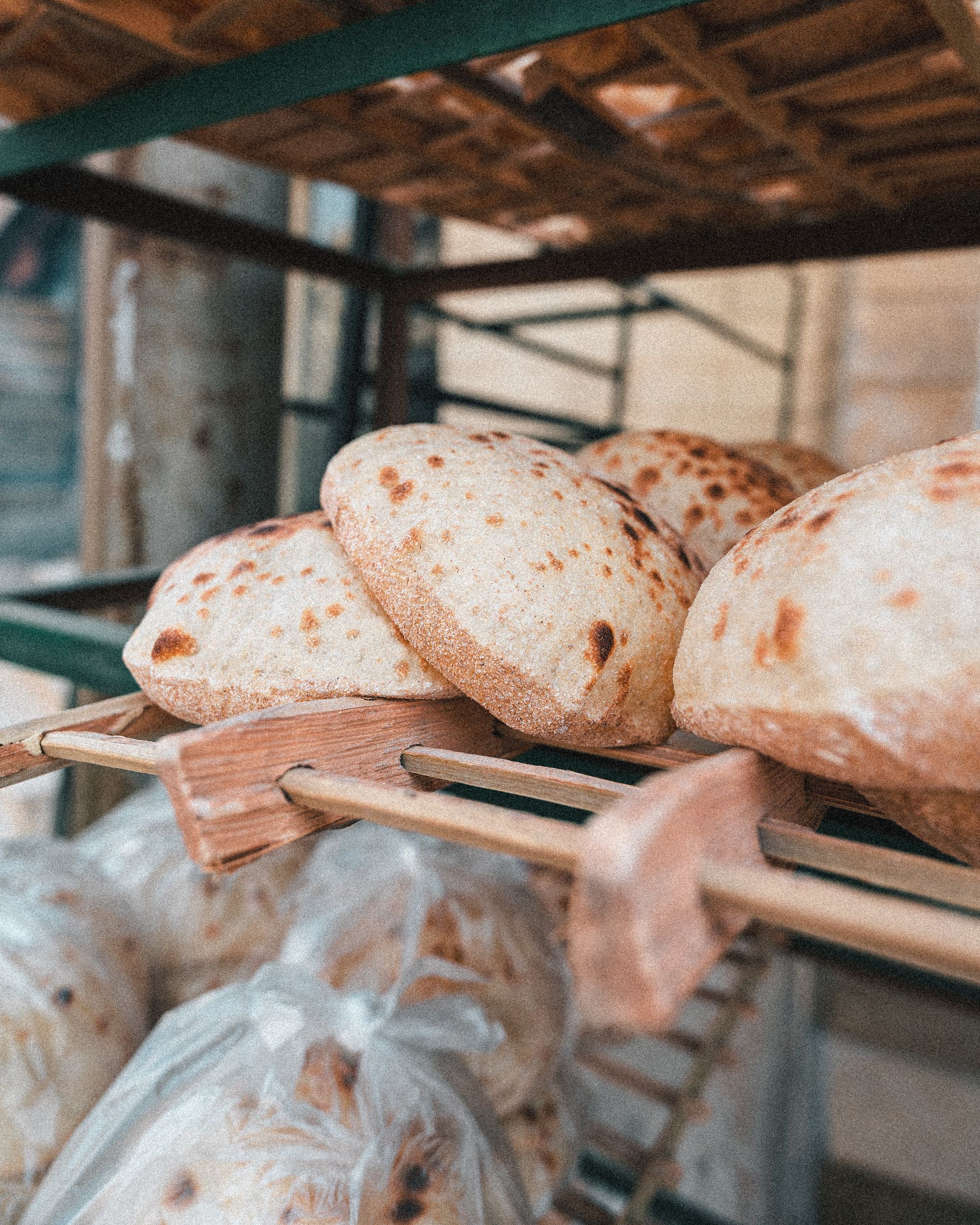 Close-up of freshly baked Egyptian flatbread cooling on wooden racks in a Cairo bakery.