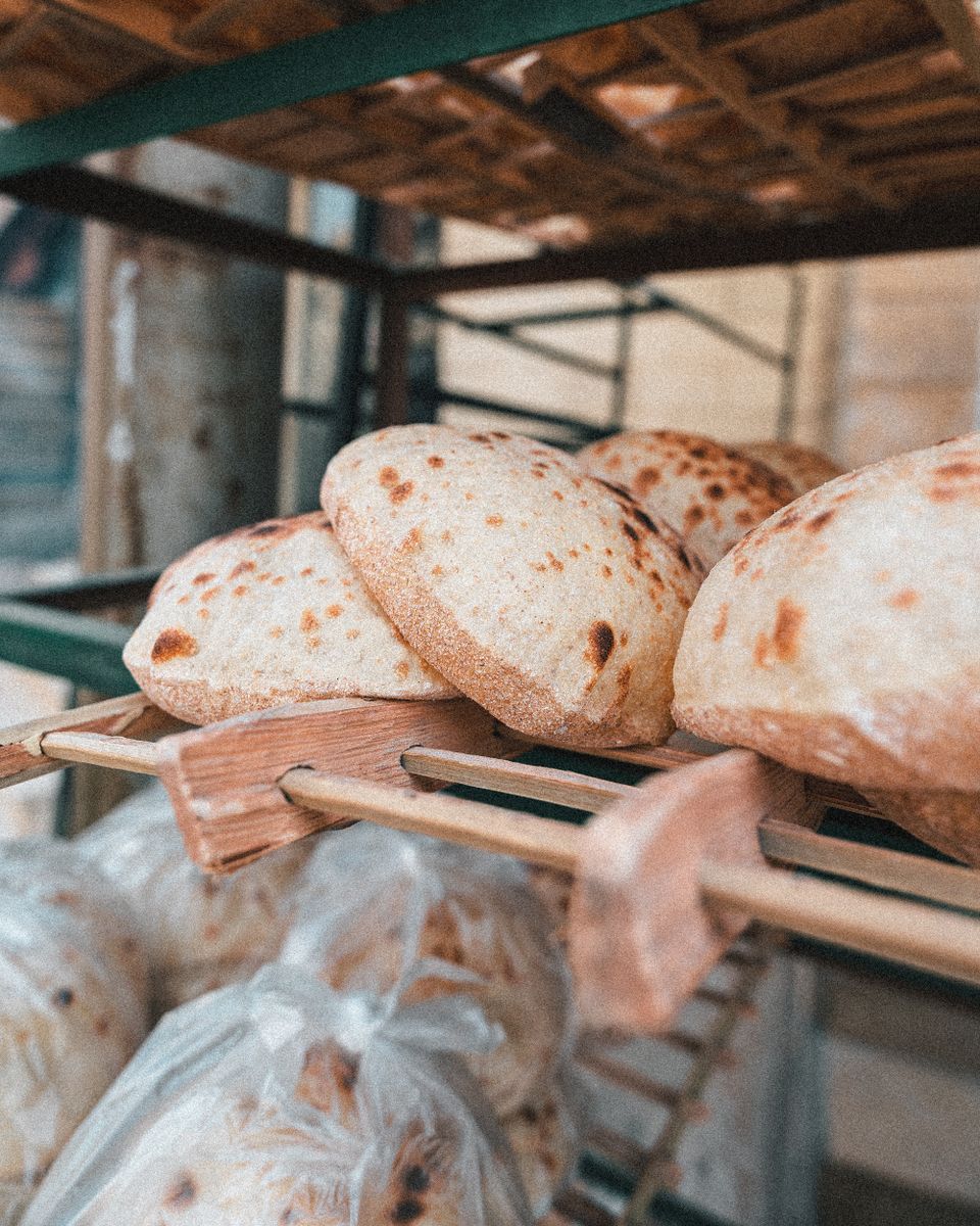 Freshly baked golden brown flatbreads, possibly pita, stacked on a wooden rack at a market stall.