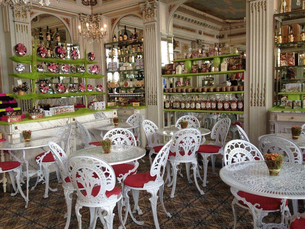 Ornate interior of a classic Parisian tea room with white cast-iron tables and chairs, displaying gourmet sweets.